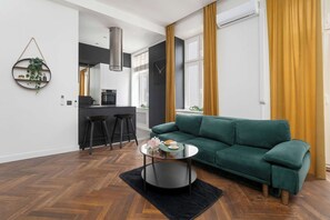 Ein modernes Wohnzimmer mit einem grünen Sofa, einem runden Couchtisch und einer Küchenzeile im Hintergrund.