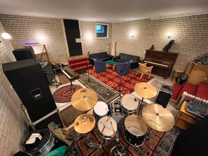 Ein Zimmer mit Backsteinwand, Klavier, Schlagzeug, Keyboard und Fernseher.