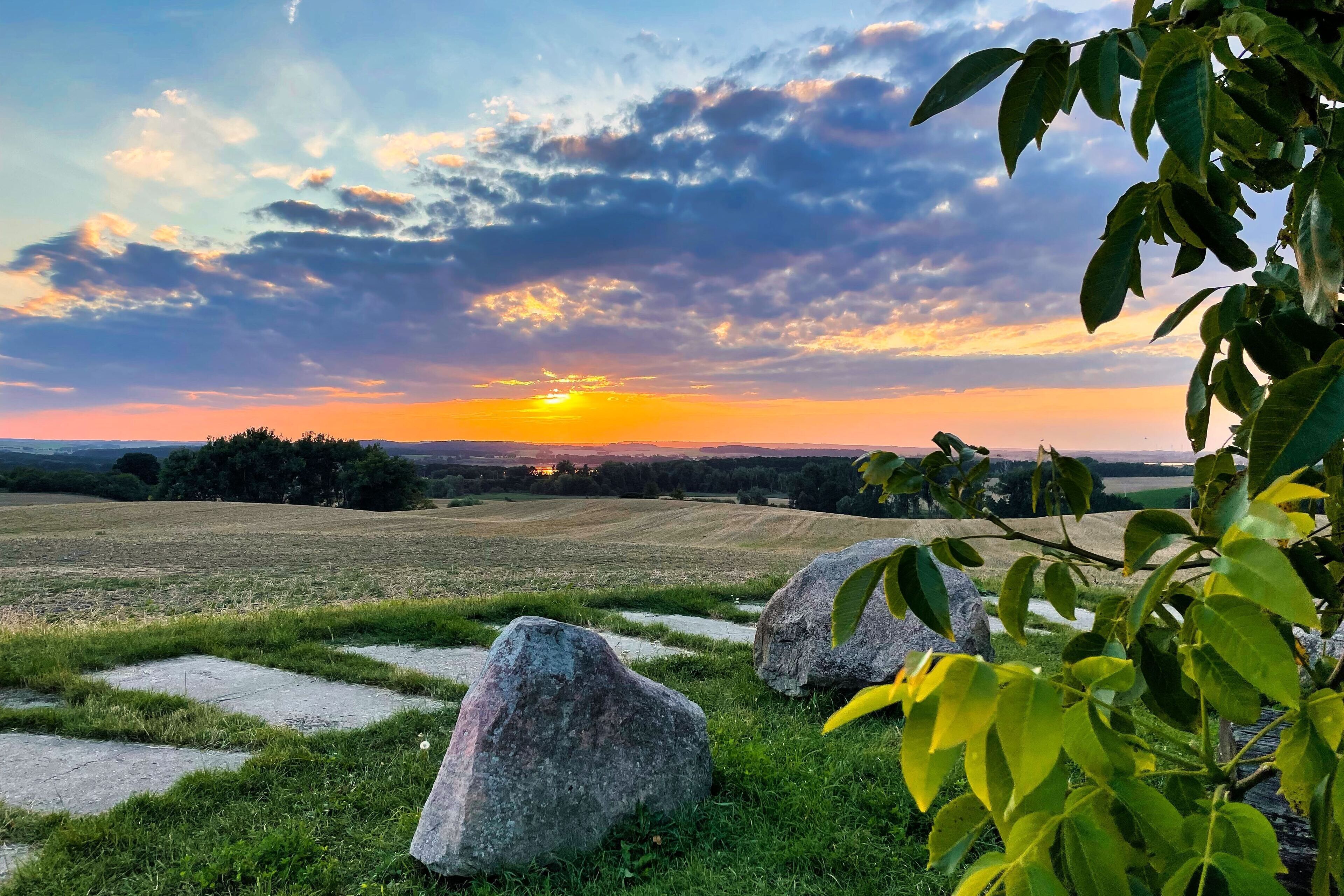 A landscape with a sunset, grassy fields, and large rocks.