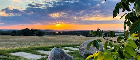 A landscape with a sunset, grassy fields, and large rocks.