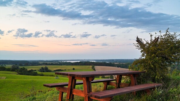 A wooden picnic table in a grassy field with a view of a distant landscape. - Cozy accommodations on Lake Oberuckersee for larger groups (Flieth-Stegelitz)