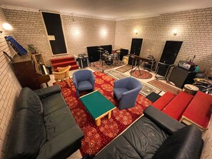 Ein Zimmer mit Backsteinwand, einem Klavier, einem Schlagzeug und einer Sitzecke mit Sofas und Sesseln.