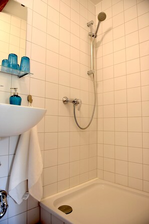 Ein Badezimmer mit einer weißen Badewanne, einer Duschbrause, einem Waschbecken mit einer blauen Flasche und einem Handtuchhalter.