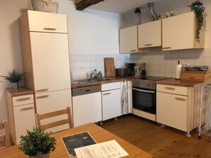 Eine kleine Küche mit weißen Schränken, einer Holz Arbeitsplatte, einem eingebauten Backofen und einem Esstisch mit Stühlen.