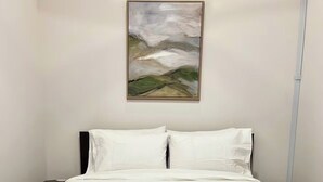 A bedroom with a bed, a green ottoman, a nightstand, and a painting on the wall. - Brick & Bed - Riverfront Loft (St. Louis)