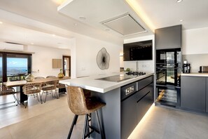 A modern kitchen with a central island, built-in appliances, and a dining area with a view. - Villa 'Carlini' with Sea View, Wi-Fi and Air Conditioning (Son Serralta)