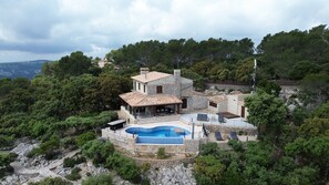 A stone villa with a swimming pool, outdoor seating, and lush greenery. - Villa 'Carlini' with Sea View, Wi-Fi and Air Conditioning (Son Serralta)