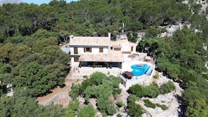 Une villa dotée d’une piscine, entourée d’une forêt dense et d’un terrain rocheux.