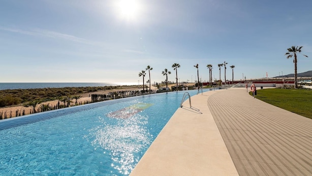 Una piscina con vista despejada al océano, un flotador salvavidas y un paseo bordeado de palmeras.