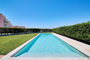 A rectangular swimming pool with clear blue water, surrounded by a well-maintained lawn and a hedge. - NEW: Coelho Apartment with Ocean View and Pool (Armação de Pêra)