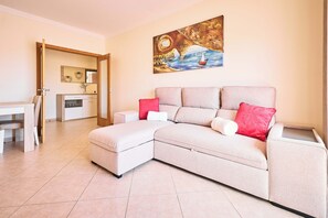A modern living room with a sectional sofa, a dining area with a table and chairs, and a painting on the wall. - NEW: Coelho Apartment with Ocean View and Pool (Armação de Pêra)
