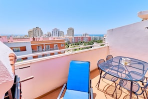 Ein Balkon mit Tisch und Stühlen, der auf eine Stadtansicht mit Gebäuden und blauem Himmel blickt.