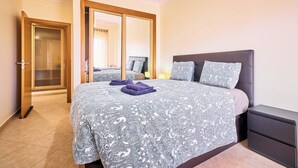 Un dormitorio con cama, mesita de noche, espejo y puerta que da a otra habitación.