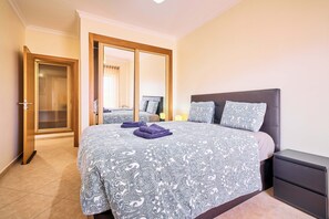 A bedroom with a bed, a nightstand, a mirror, and a door leading to another room. - NEW: Coelho Apartment with Ocean View and Pool (Armação de Pêra)