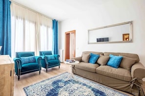 Ein Wohnzimmer mit einer Couch, zwei Sesseln, einem Couchtisch, einem gemusterten Teppich, einem großen Spiegel und einer Tür.