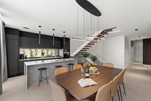 A modern kitchen with a central island, a dining area with a wooden table, and a staircase leading to an upper level. - Villas Parenzo II (Kukci)