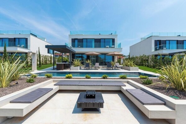 Une maison moderne dotée d’une piscine, d’un espace salon extérieur et d’un coin barbecue.