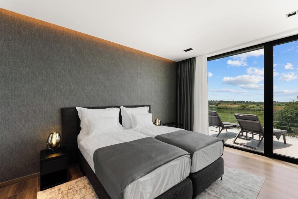 Une chambre d’hôtel moderne dotée d’un grand lit, d’une table de chevet, d’une vue sur l’extérieur et d’un balcon avec des chaises.
