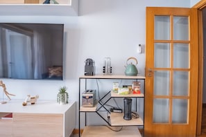 Una cocina moderna con tostadora, hervidor y cafetera sobre la encimera, una puerta de madera con paneles de vidrio esmerilado y un televisor montado en la pared.
