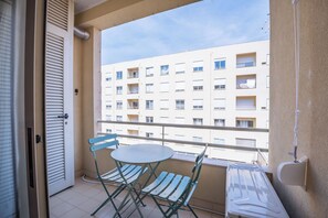 Un balcon avec une table et des chaises, une fenêtre et une vue sur un immeuble doté de nombreuses fenêtres et de balcons.