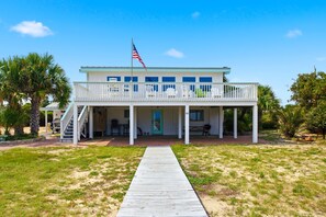 A two-story house with a covered porch and a flagpole. - Welcome to Sisters By The Sea! (St. George Island)