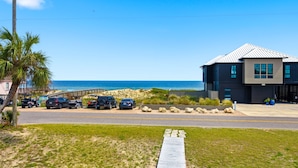Um edifício moderno com cobertura metálica, área de estacionamento com vários carros e vista para a praia e oceano.