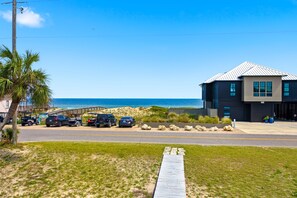 A modern building with a metal roof, a parking area with several cars, and a view of the beach and ocean. - Welcome to Sisters By The Sea! (St. George Island)