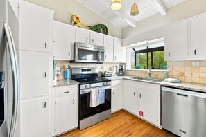 A modern kitchen with white cabinetry, stainless steel appliances, and a large window providing natural light. - Welcome to Sisters By The Sea! (St. George Island)
