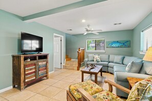 A living room with a television on a wooden cabinet, a sofa, a coffee table, and a ceiling fan. - Welcome to Sisters By The Sea! (St. George Island)