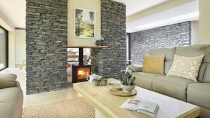 A living room with a stone fireplace, a sofa, a coffee table, and a cactus plant. - Fawns Keep - Hot Tub & Sauna Retreat | Ridgestone (Bowness-on-Windermere)