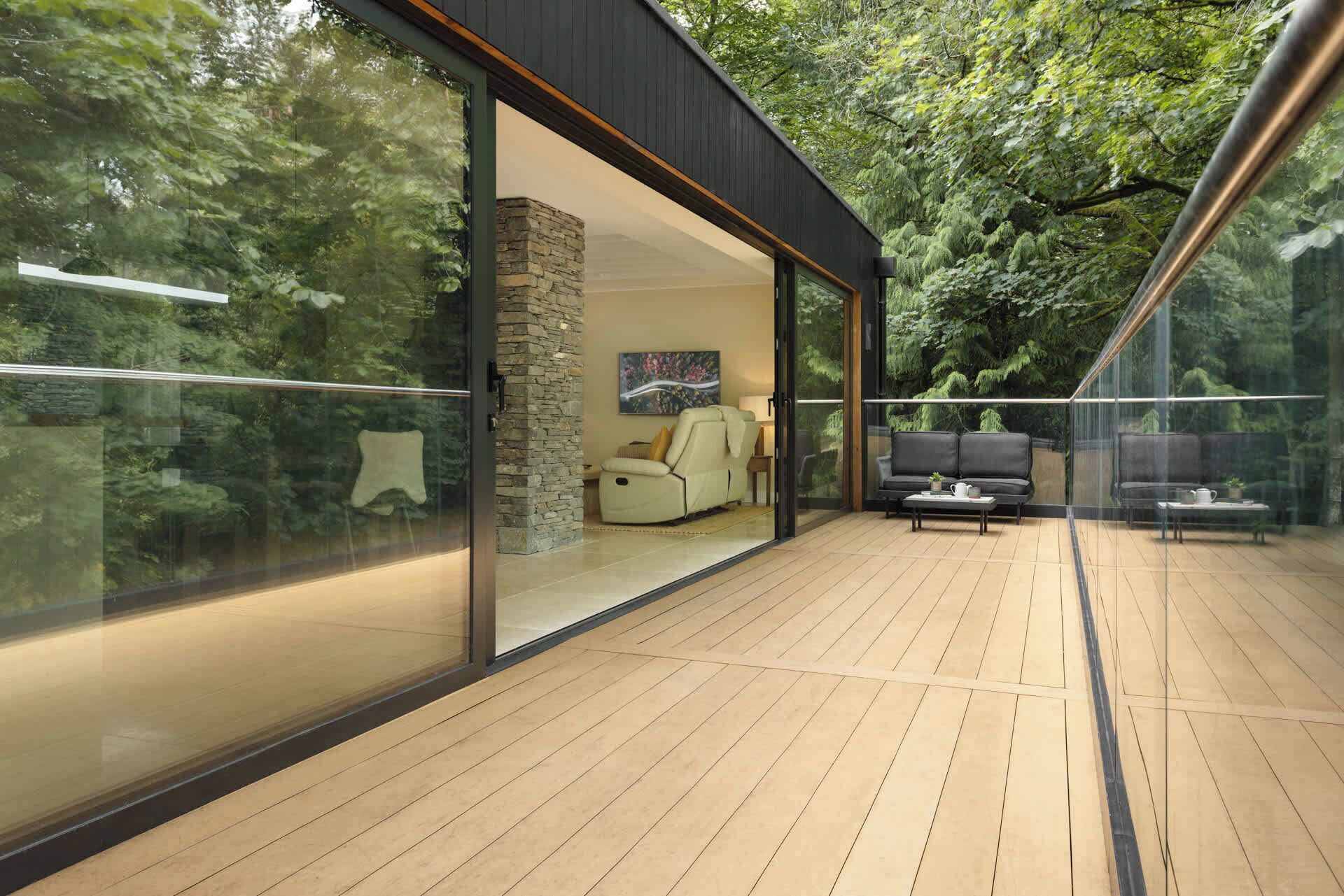 A modern outdoor living space with a glass wall, wooden flooring, and a stone pillar.