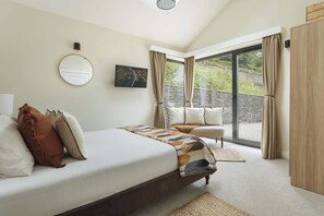 Une chambre avec un lit, un canapé, une grande fenêtre et une vue sur la verdure.