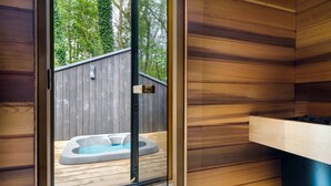 A wooden cabin with a glass door leading to a deck area featuring a hot tub. - Fawns Keep - Hot Tub & Sauna Retreat | Ridgestone (Bowness-on-Windermere)