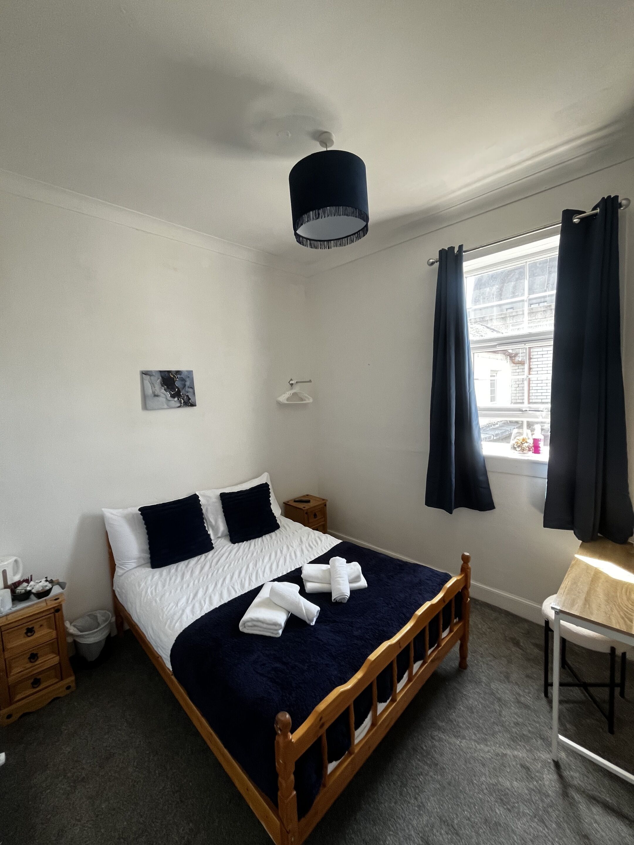 Une chambre à coucher avec un lit, une table de chevet, une commode et une fenêtre avec des rideaux.