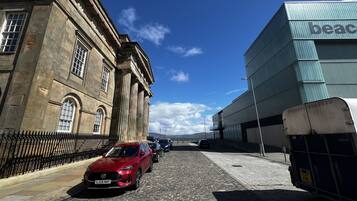 Une rue pavée avec une voiture rouge garée sur le bord, un bâtiment historique orné de colonnes et un bâtiment moderne dont la façade porte l'inscription « beac ».