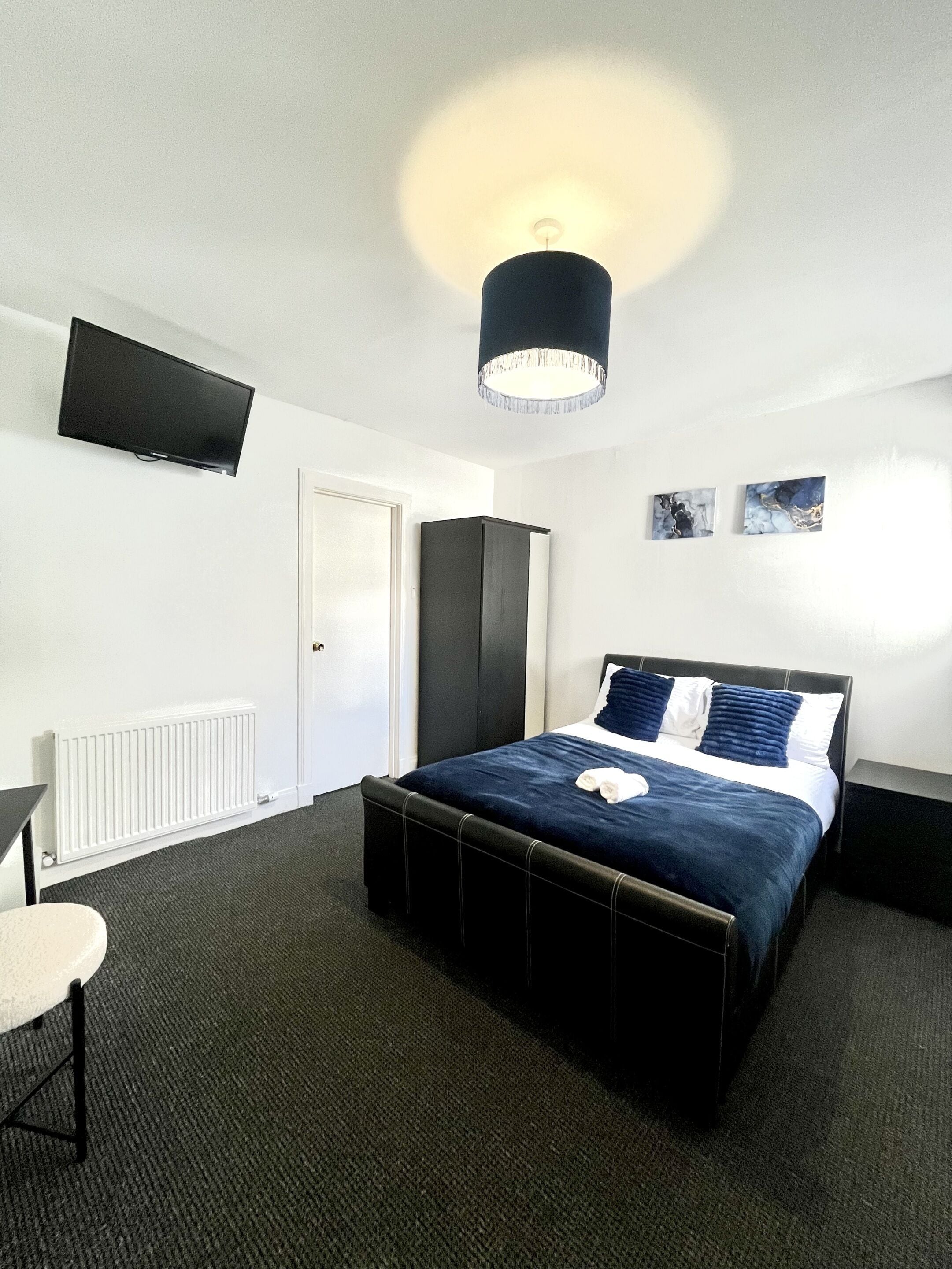 A bedroom with a bed, a flat-screen TV, a radiator, a wardrobe, and artwork on the wall.