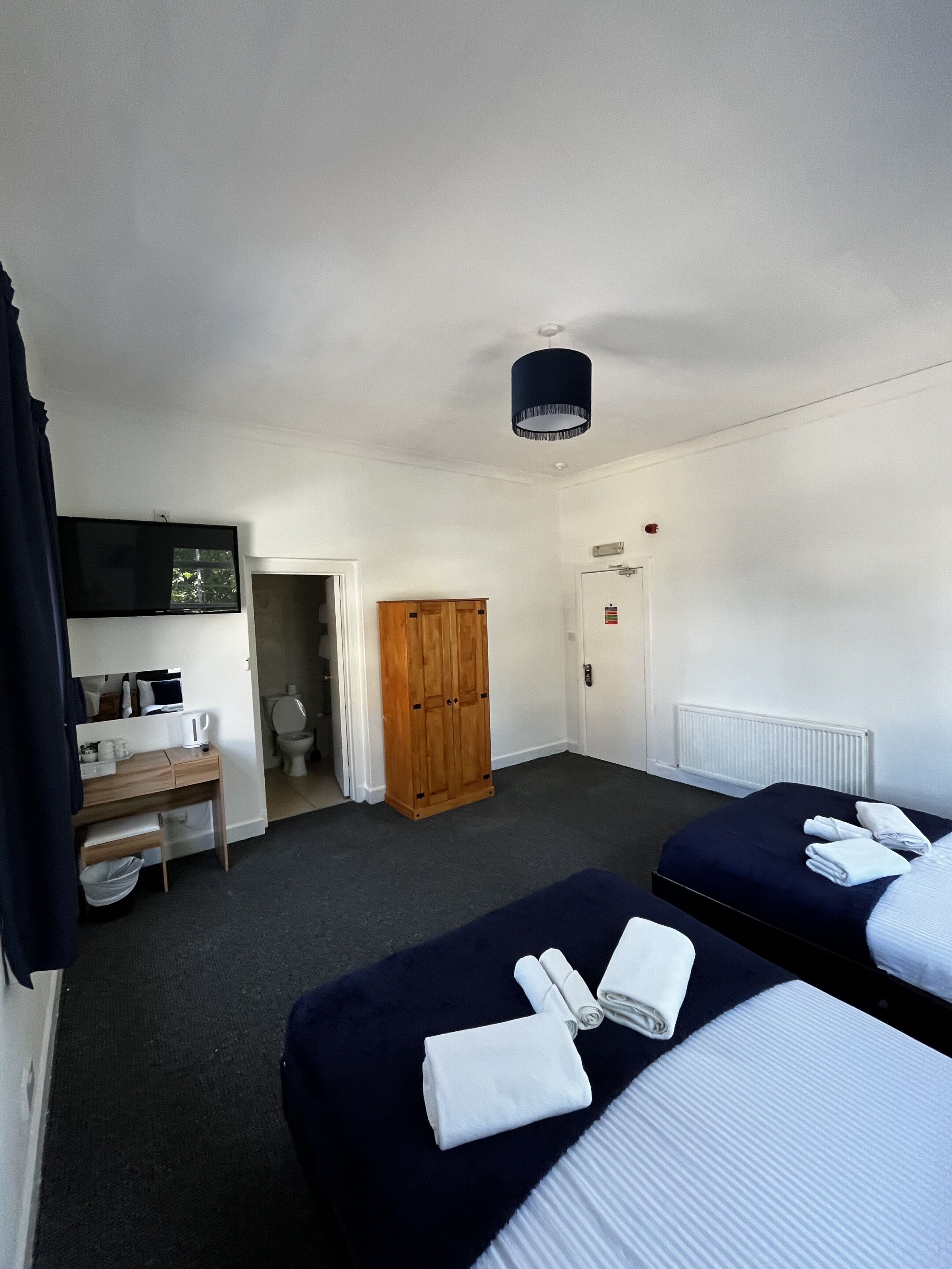 Una camera d'albergo con due letti, una scrivania con una sedia, una televisione, un armadio e un bagno.