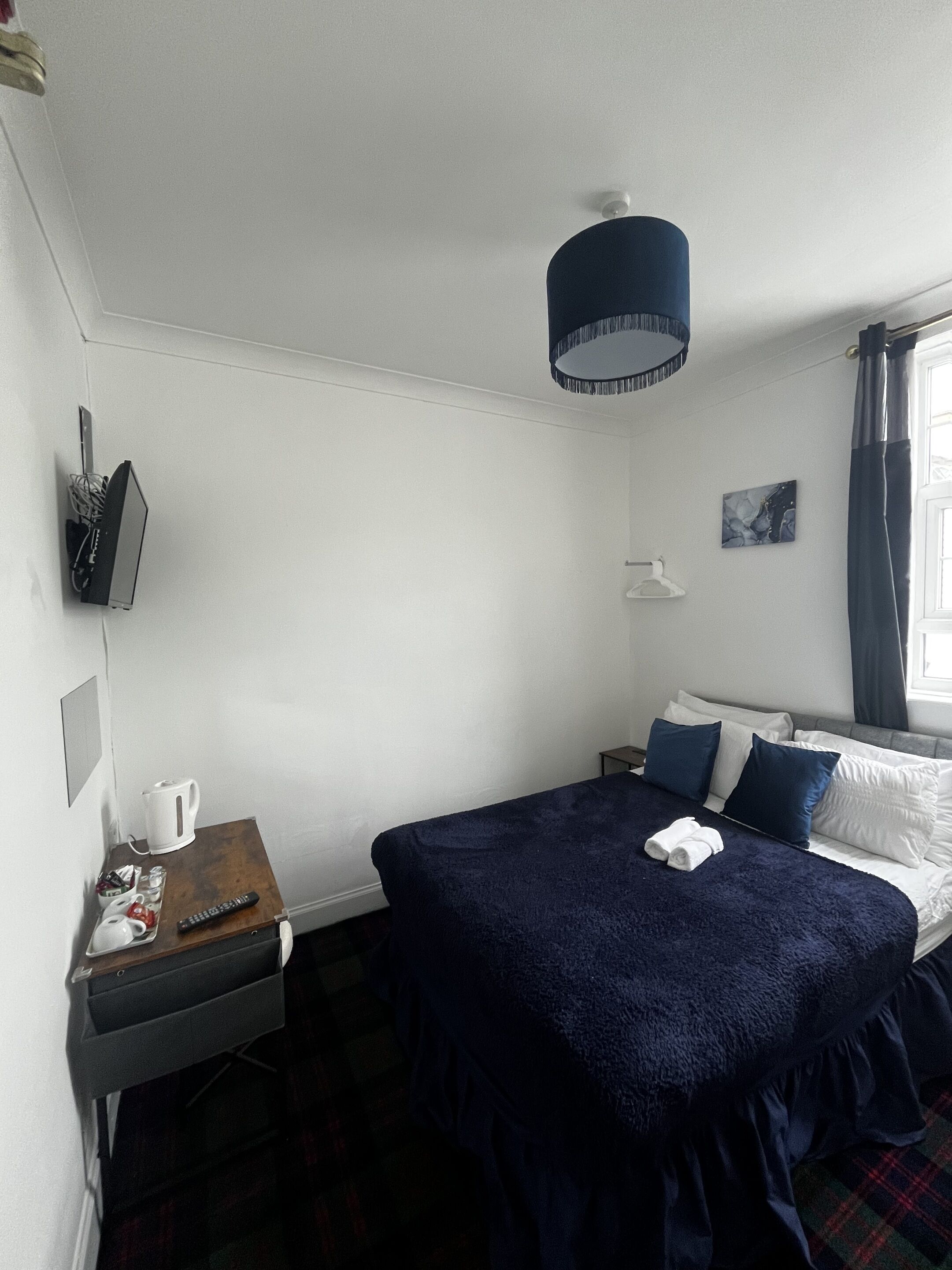 A hotel room with a bed, bedside table, lamp, and a window with curtains.