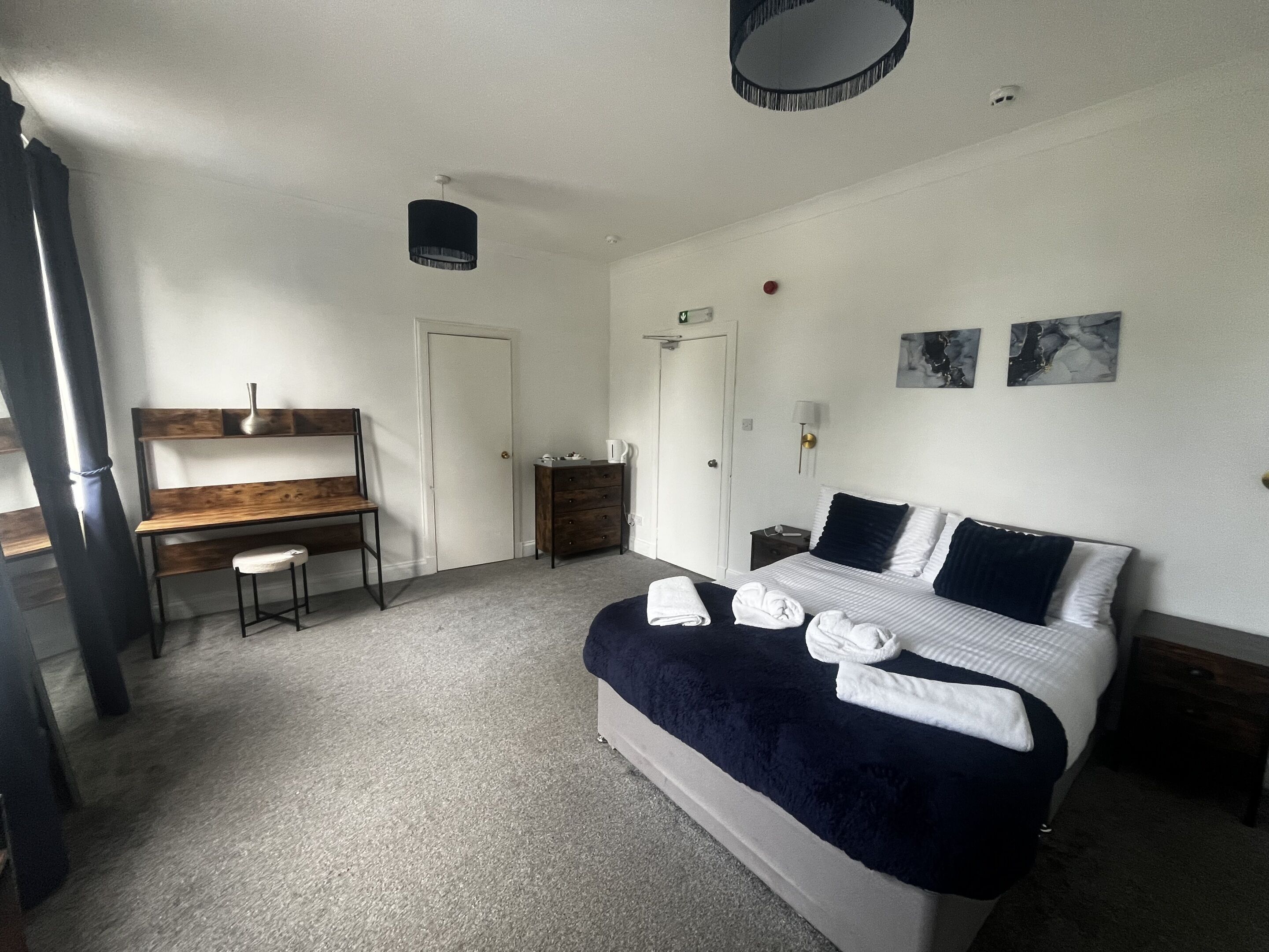 A bedroom with a bed, a desk, a chair, a dresser, and a door.