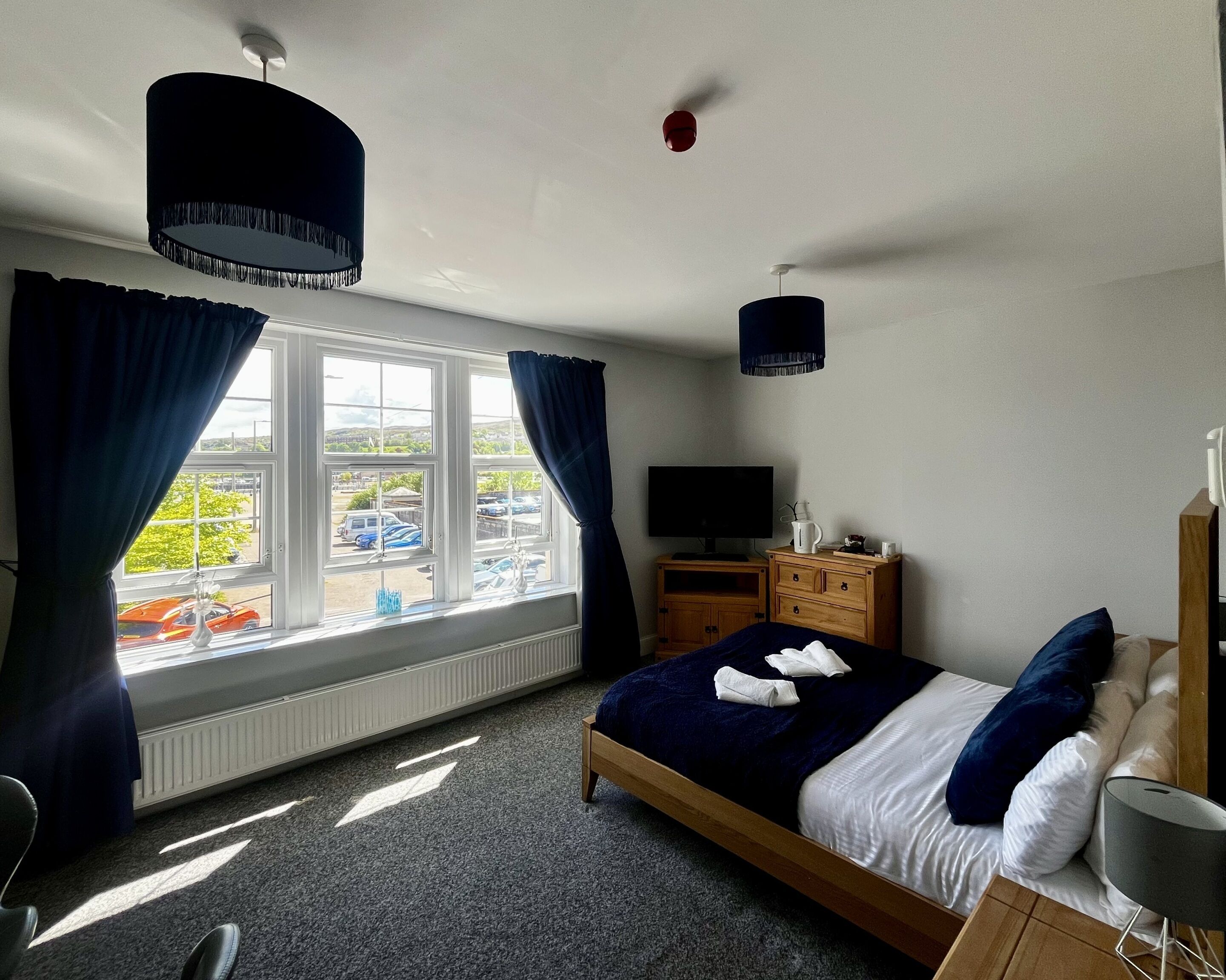A bedroom with a bed, a TV, a dresser, and a window with curtains.