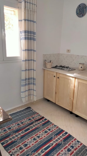 A kitchen with wooden cabinets, a gas stove, a sink, and a window with curtains.