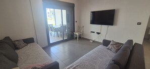 A living room with two sofas, a TV mounted on the wall, and a sliding glass door leading to an outdoor area with chairs. - Groundfloor, oasis beach 2 la zenia (La Zenia)