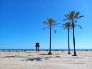 Ein Strand mit Palmen, einem Rettungsturm und Sonnenschirmen.