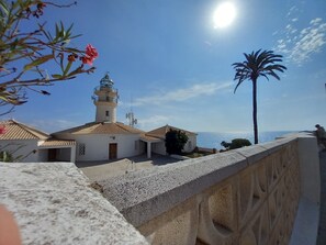 Un edifici costaner amb un far, una palmera i un cel serè.