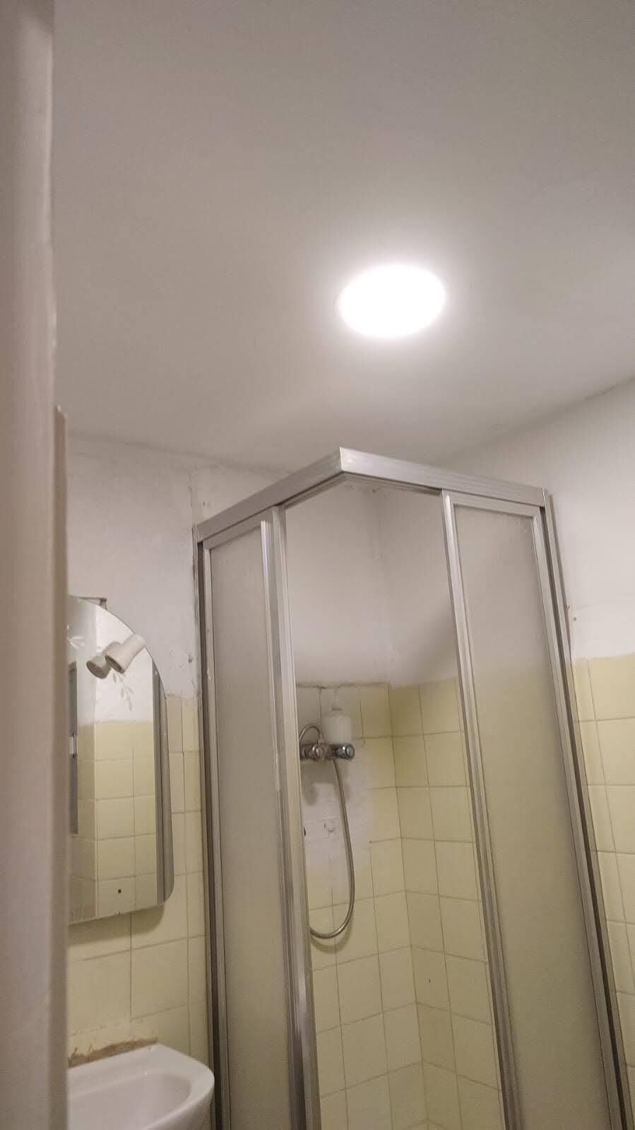 A corner shower with a glass door, a white sink, and a mirror.