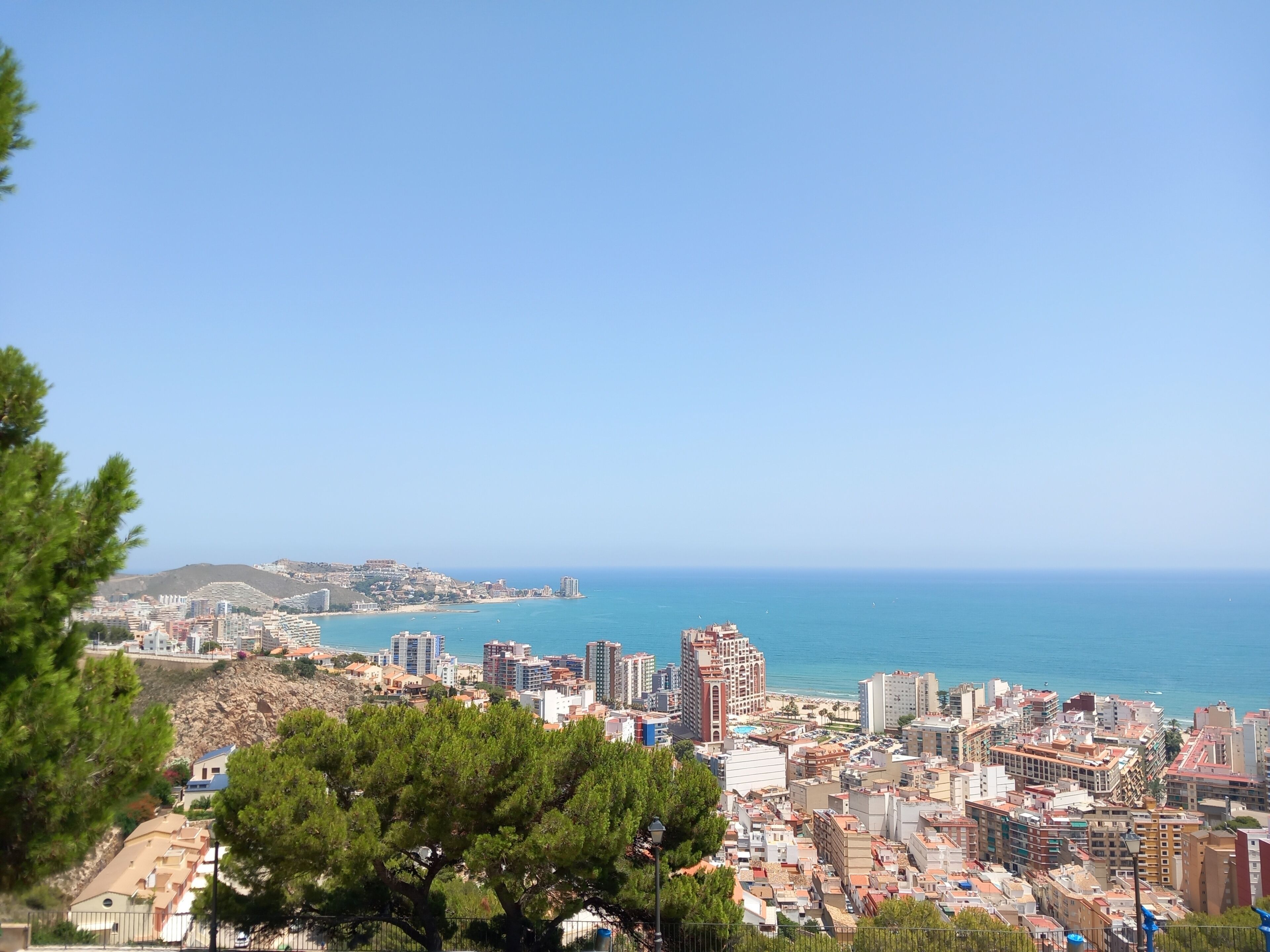 A coastal cityscape with dense urban buildings, a prominent hotel with a red facade, and a clear view of the sea.