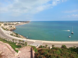 Carretera costanera amb pas de vianants, un camí de pedra i vista al mar amb vaixells.