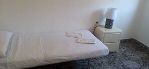 Ein Einzelbett mit weißen Bettwäsche und zwei gefalteten Handtüchern, eine Nachttischlampe und ein kleiner, weißer Nachttisch.
