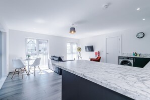 A modern kitchen with a marble countertop, a dining area with a white chair, and a large window. - Stylish 2BDR Hospitals Nearby Free Parking (Liverpool)