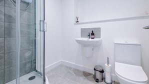 Un baño moderno con cabina de ducha de vidrio, un lavamanos blanco y un inodoro.